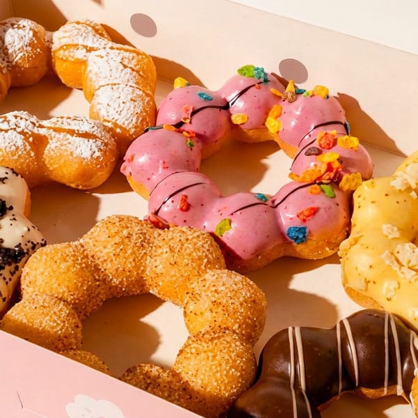 Assorted mochi donuts with various colorful glazes and toppings in a pink box.