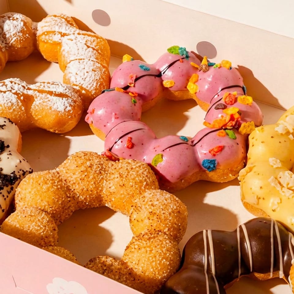 Assorted mochi donuts with various colorful glazes and toppings in a pink box.
