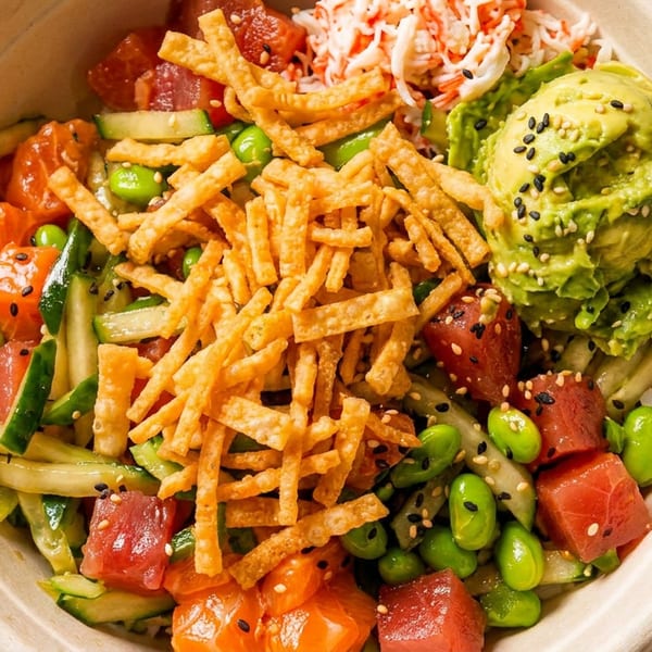 Colorful poke bowl with tuna, salmon, avocado, edamame, cucumber, crab, and crispy toppings.