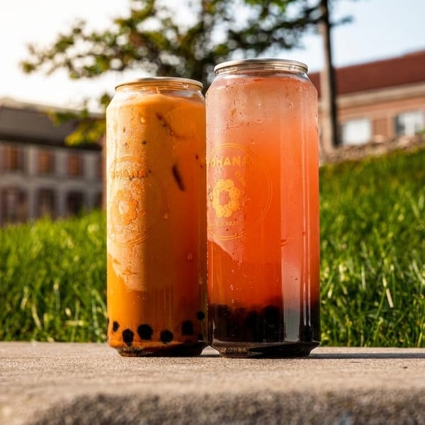 Ohana canned boba drinks, one orange and one red, on a concrete surface outdoors.