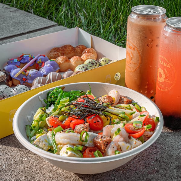 A poke bowl with shrimp, tuna, and vegetables, a box of colorful mochi donuts, and two canned drinks.