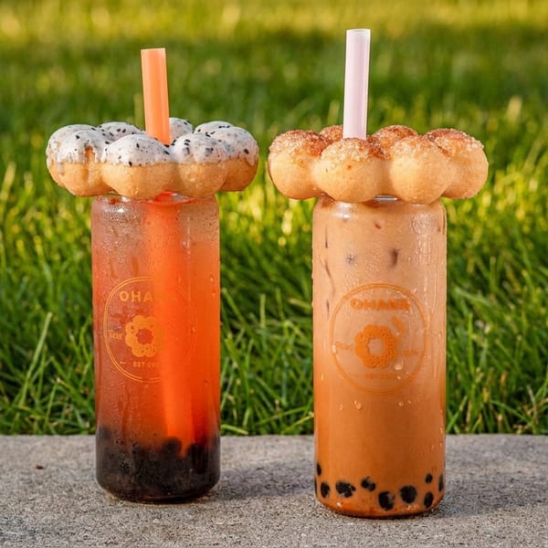 Two Ohana boba drinks, one with dragon fruit donut and one with cinnamon sugar donut, on concrete with grass.