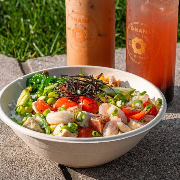 Colorful poke bowl with shrimp, tuna, and vegetables, plus two Ohana branded drinks outdoors.