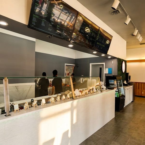 Bright, modern restaurant interior featuring a service counter, digital menus, and a green accent wall.